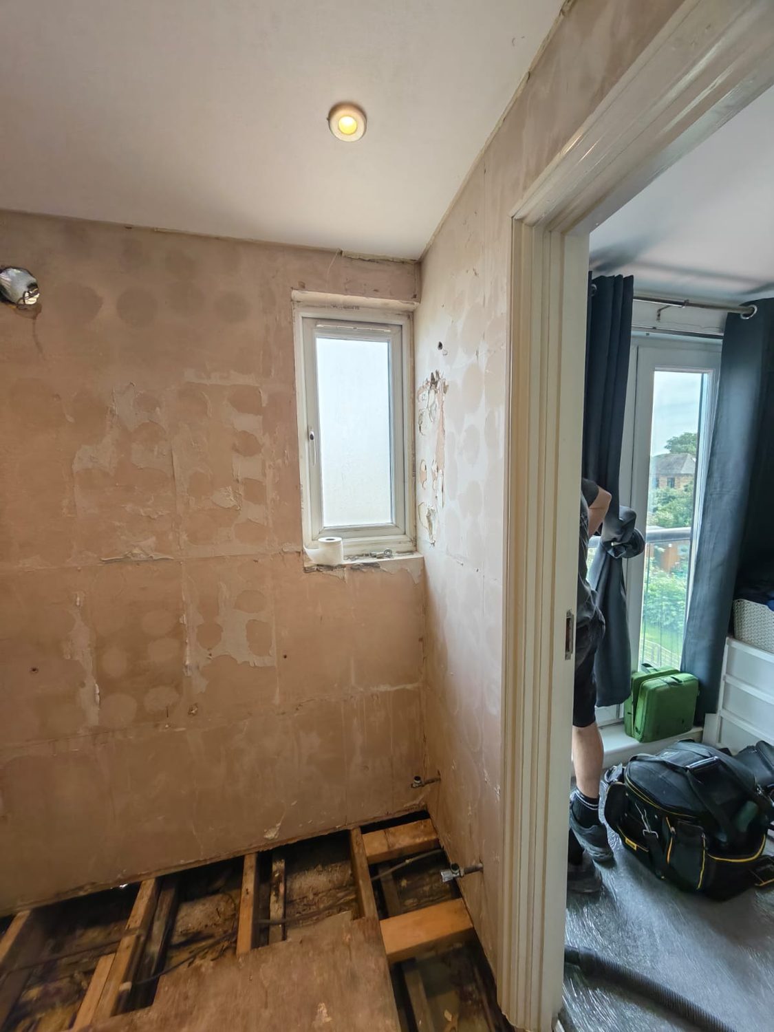 Bathroom stripped to bare plaster with the floorboards lifted and joists exposed