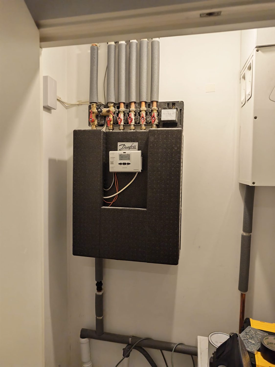 Wall-mounted Danfoss heat interface unit with its insulated cover on and a Kamstrup heat meter display
