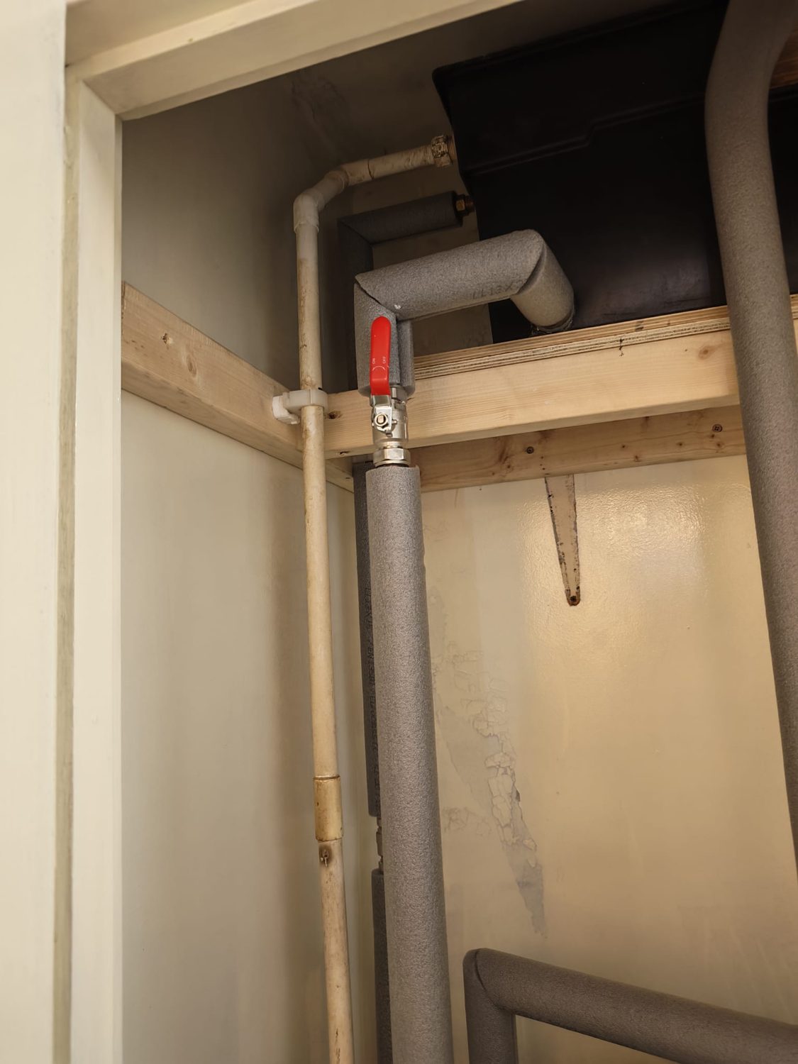 A cupboard rebuilt with newly insulated pipework, a red lever isolating valve and a timber support frame